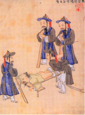 A male-presenting person surrounded by uniformed guards holding wooden paddles is tied belly-down to a cross-shaped wooden frame with his pants pulled down to expose his buttocks.