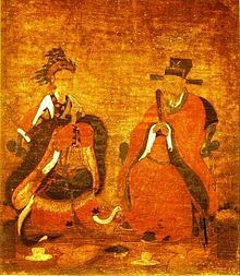 A painting in tones of red and brown of a man and woman in flowing robes facing each other, the woman in a wavy headdress and the man wearing a horsehair hat.