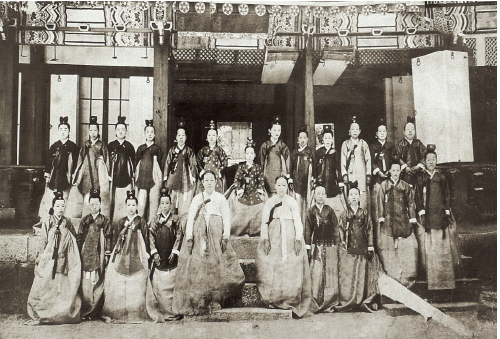 A black-and-white group photograph of women posed before a building in long tops and skirts wearing headdresses.